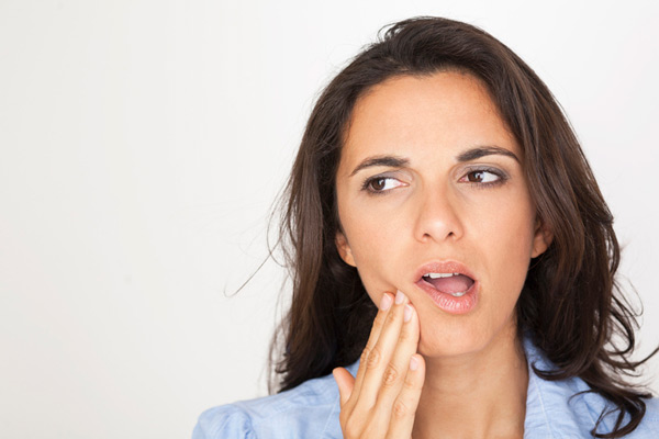 Mujer sosteniéndose la mejilla por dolor en los dientes.